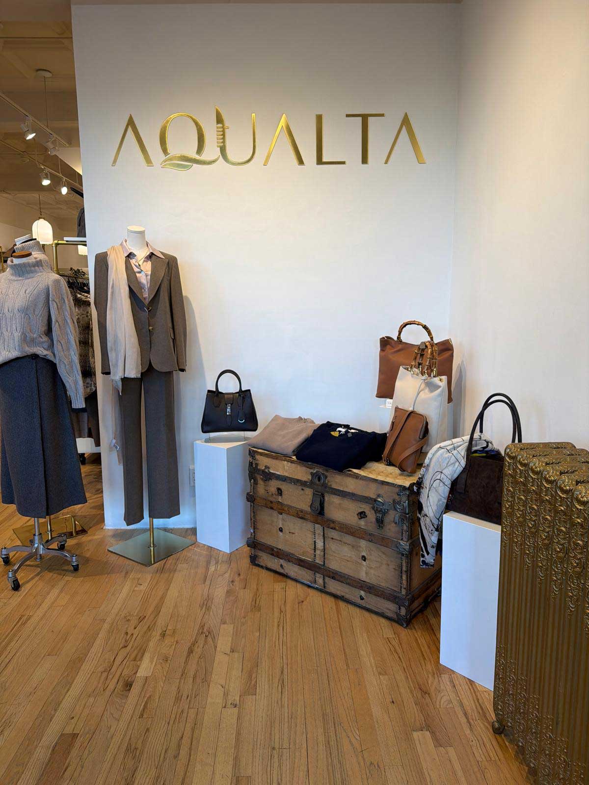 Inside Aqualta boutique with clothing racks, display tables and a long wood checkout counter.
