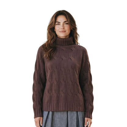 Woman wearing a cable knit cashmere turtleneck sweater in brown by Sand, sold at Aqualta, styled with a pleated gray skirt.