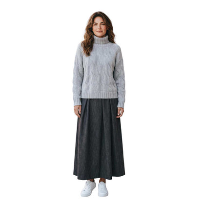 Woman wearing a cable knit cashmere turtleneck sweater in oatmeal by Sand, sold at Aqualta, styled with a long dark skirt and white sneakers.