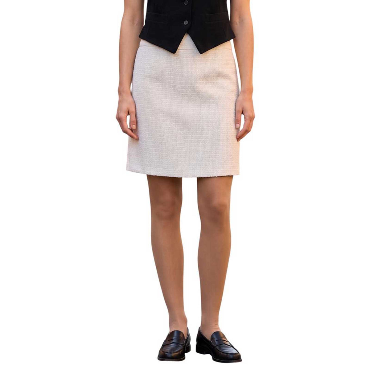 Model wearing SAND cream tweed above-the-knee skirt with a black tailored vest and loafers, available at Aqualta.