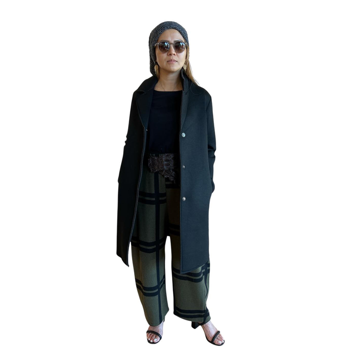 Person wearing a long black coat, black top, and patterned pants on a white background