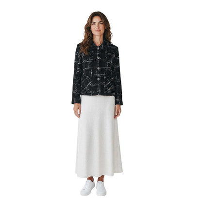 Woman wearing a short collar jacket in black and white tweed by Sand, sold at Aqualta, styled with a long white skirt and white sneakers.
